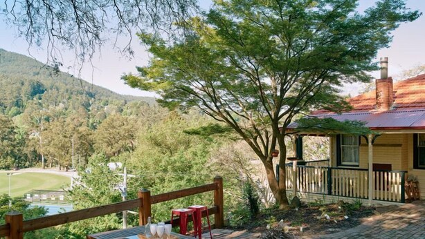 A wooden deck with a table and benches, surrounded by greenery and a view of a golf course and hills. - Ada Cottage - Warburton, Yarra Valley (Warburton)