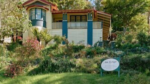 A two-story house with a balcony, surrounded by lush greenery and trees. - Ada Cottage - Warburton, Yarra Valley (Warburton)