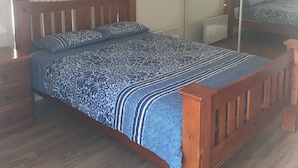 Une chambre à coucher avec un lit en bois, une table de chevet, un miroir et une fenêtre avec des stores.