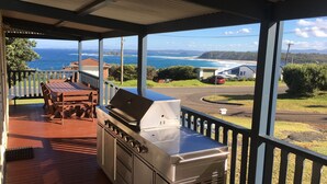 Un espace extérieur abrité, doté d’un barbecue et d’une table, offrant une vue sur la côte.