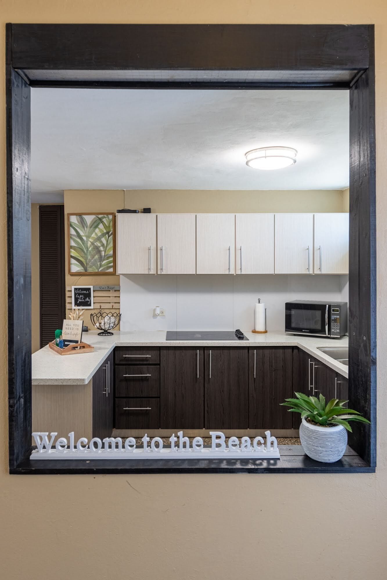 A kitchen with white cabinets, a microwave, and a welcome sign.