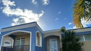 Ein Wohnhaus mit blauer Fassade, einer weißen Tür und einer kleinen Veranda mit Geländer.
