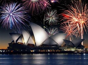 Sydney Opera House shines against the night sky, its iconic architecture reflected in the water below.