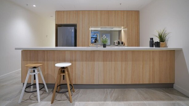 A modern kitchen with a wooden countertop, two stools, and a refrigerator.