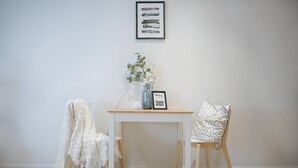 A room with a white table, two chairs, a vase with flowers, and a framed picture on the wall.