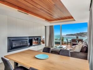A modern living room with a TV, dining table, and a view of the ocean.