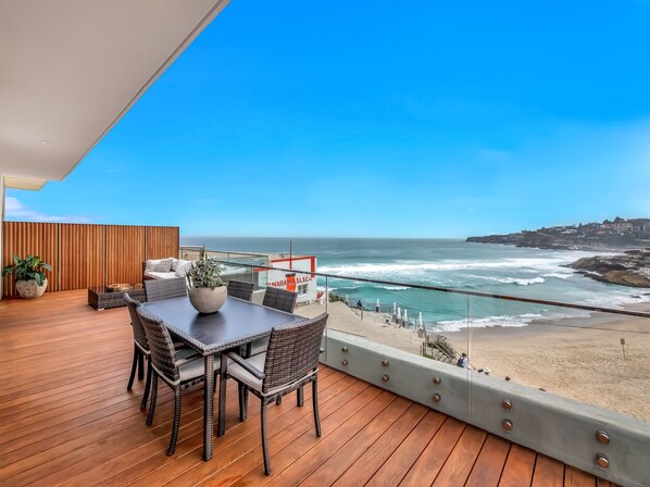 A wooden deck with a table and chairs overlooking a beach and ocean.