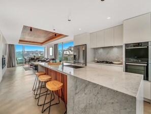 A modern kitchen with a large island, bar stools, stainless steel appliances, and a view of the city.