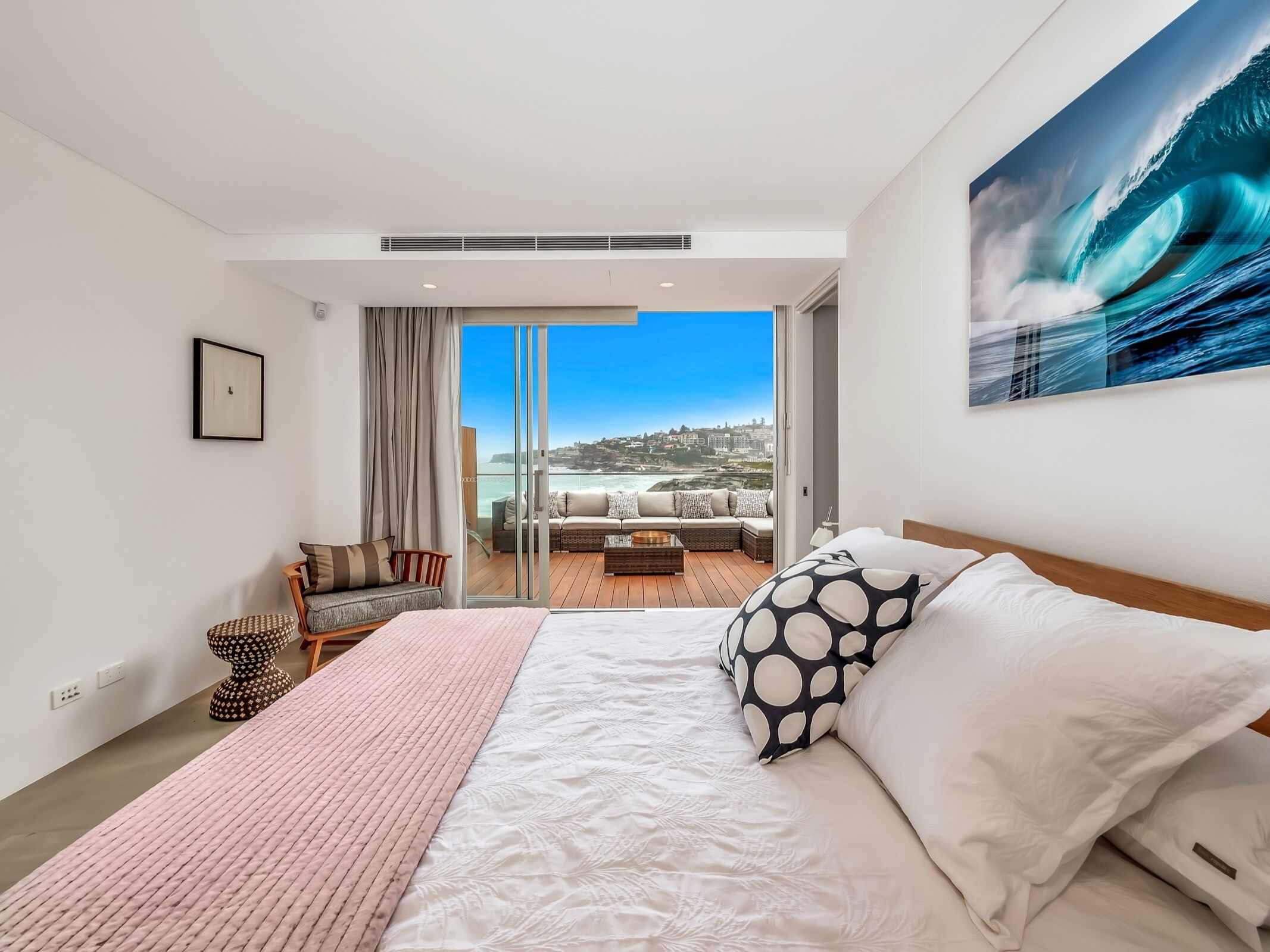 A modern bedroom with a large bed, a view of the ocean, and a balcony with outdoor seating.