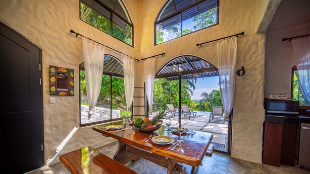 Comedor con mesa de madera dispuesta para cuatro, un frutero y vistas al exterior.