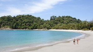 Una playa con agua turquesa cristalina, una orilla arenosa y un denso follaje verde al fondo.
