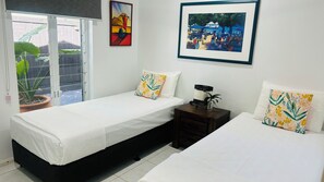 A bedroom with two beds, a window with a view of a garden, and artwork on the walls.
