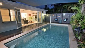 A modern outdoor pool area with a glass-enclosed patio, a wooden deck, and a fenced garden. - Bella Leuca family getaway (Port Douglas)