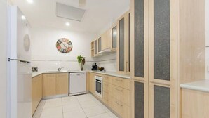 A modern kitchen with light wood cabinets, a dishwasher, and a clock on the wall. - Bella Leuca family getaway (Port Douglas)