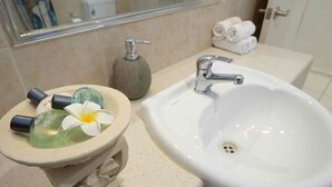 A bathroom with a white sink, a small stone basin with toiletries, and a mirror above the sink. - Bella Leuca family getaway (Port Douglas)