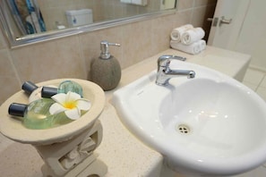 Une salle de bain avec un lavabo blanc, un petit récipient en pierre contenant des articles de toilette et un miroir au-dessus du lavabo.