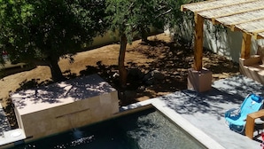 Una piscina con agua cristalina, rodeada de un patio con una pérgola y un sillón de descanso azul.