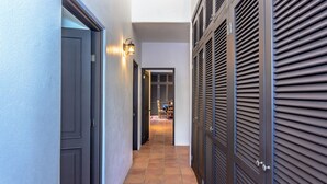 Un pasillo con suelo de baldosas, una puerta cerrada a la izquierda y un conjunto de puertas con listones a la derecha.