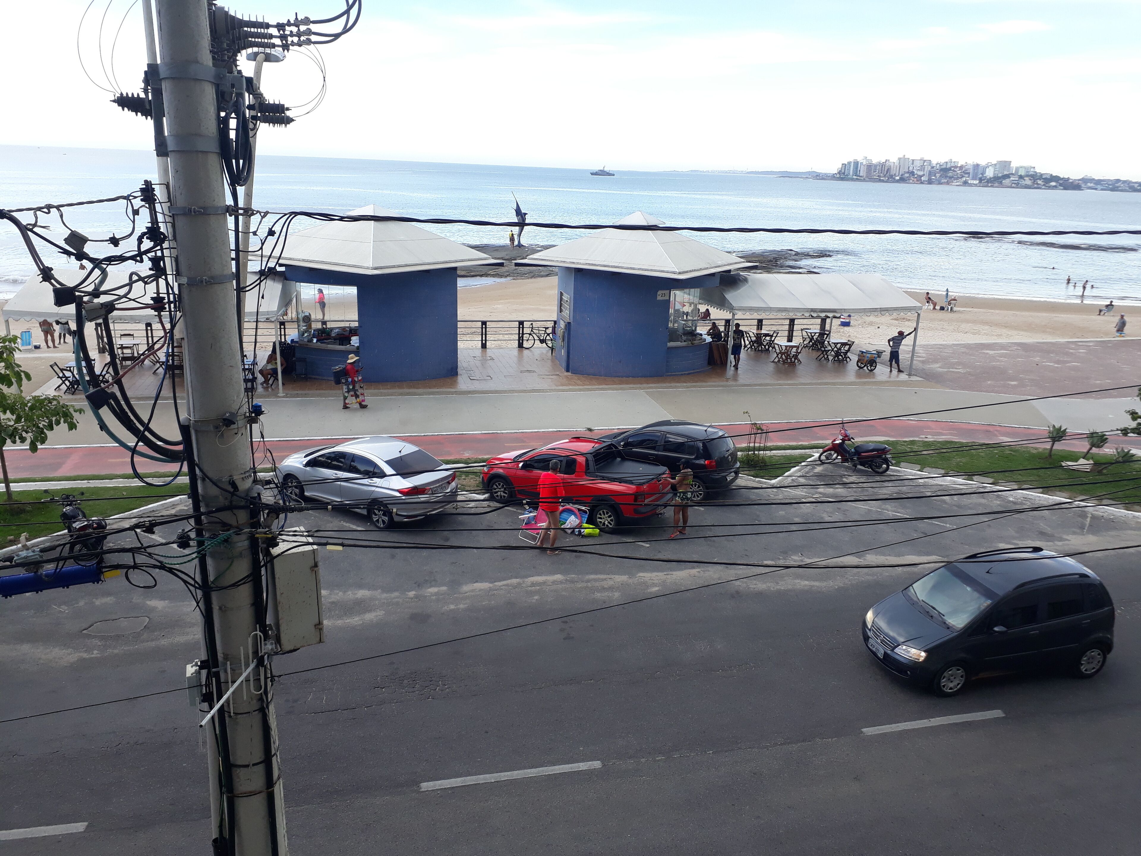 A coastal area with a beach, a parking lot, and a city skyline in the background.