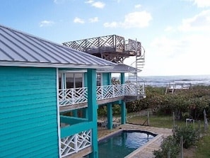 Uma casa turquesa de dois andares com uma varanda e uma piscina pequena.