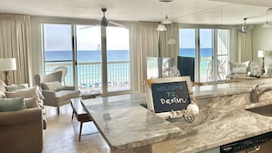 Un vaste salon avec une grande fenêtre donnant sur la mer, un îlot de cuisine en marbre et une enseigne sur laquelle on peut lire : « BIENVENUE À Destin ».