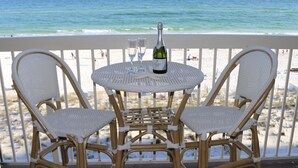 Un balcon avec des fauteuils en osier et une table ronde, donnant sur une plage avec l’océan en toile de fond.