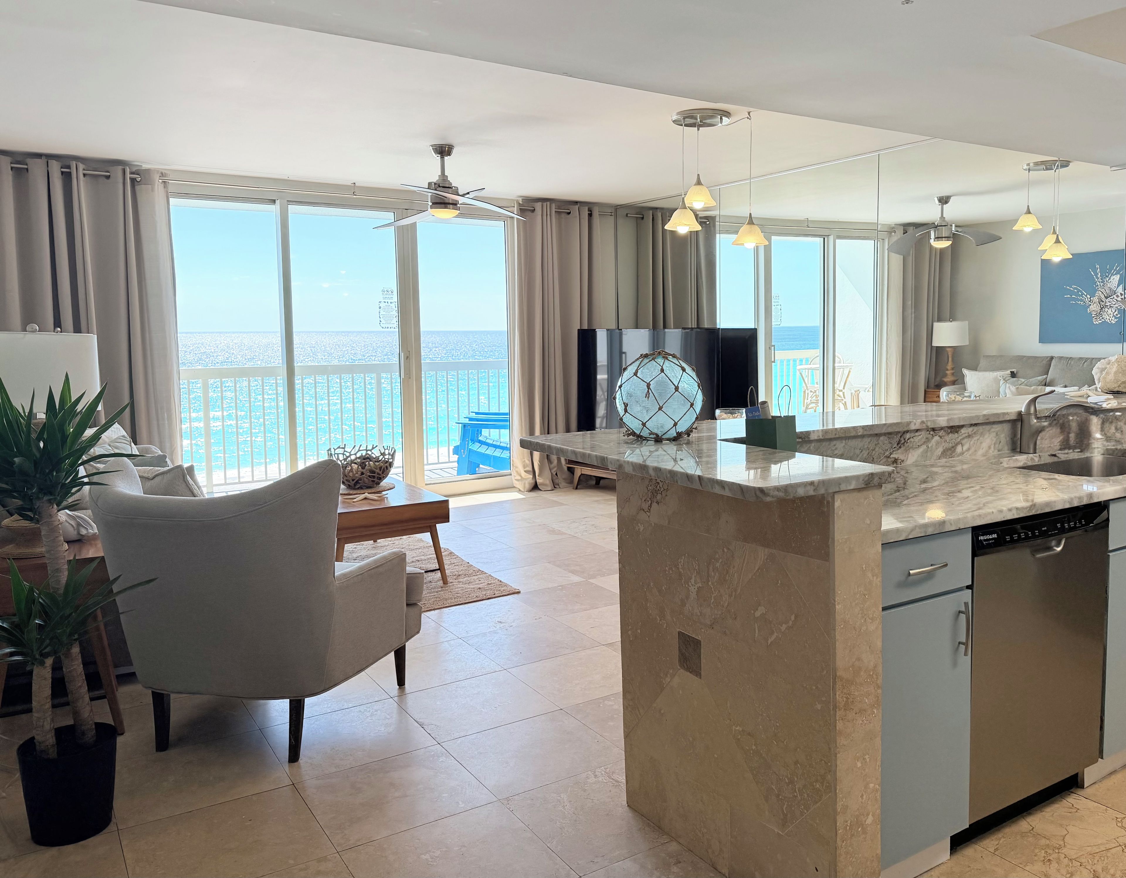 A modern kitchen with a central island, a dining area with a view, and a living space with a sofa and plants.