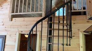 A wooden interior with a spiral staircase and a hanging light fixture. - Paradox Lake - The Carriage House   (Severance)