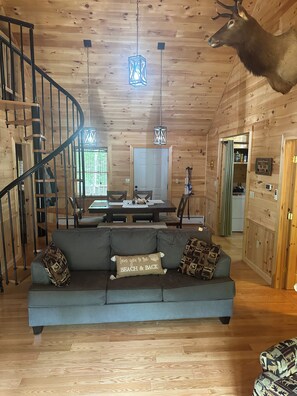 A cabin interior with a wooden interior, a dining area, a sofa with decorative pillows, and a mounted deer head.
