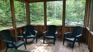 A wooden deck with four Adirondack chairs and a table, overlooking a forested area. - Paradox Lake - The Carriage House   (Severance)