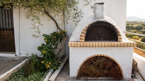 Un horno de ladrillo tradicional integrado en una pared blanca, con vistas al campo al fondo.