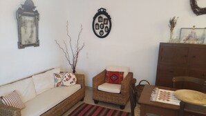 Una sala de estar con un sofá de mimbre, un sillón pequeño, una mesa de comedor con sillas y una alfombra a rayas rojas y negras.