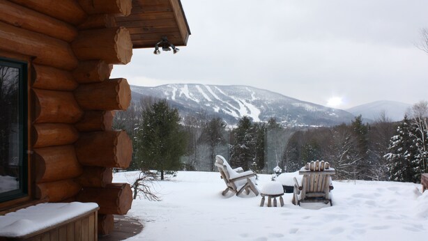 Una cabaña de troncos con un porche cubierto de nieve y zona de estar al aire libre.