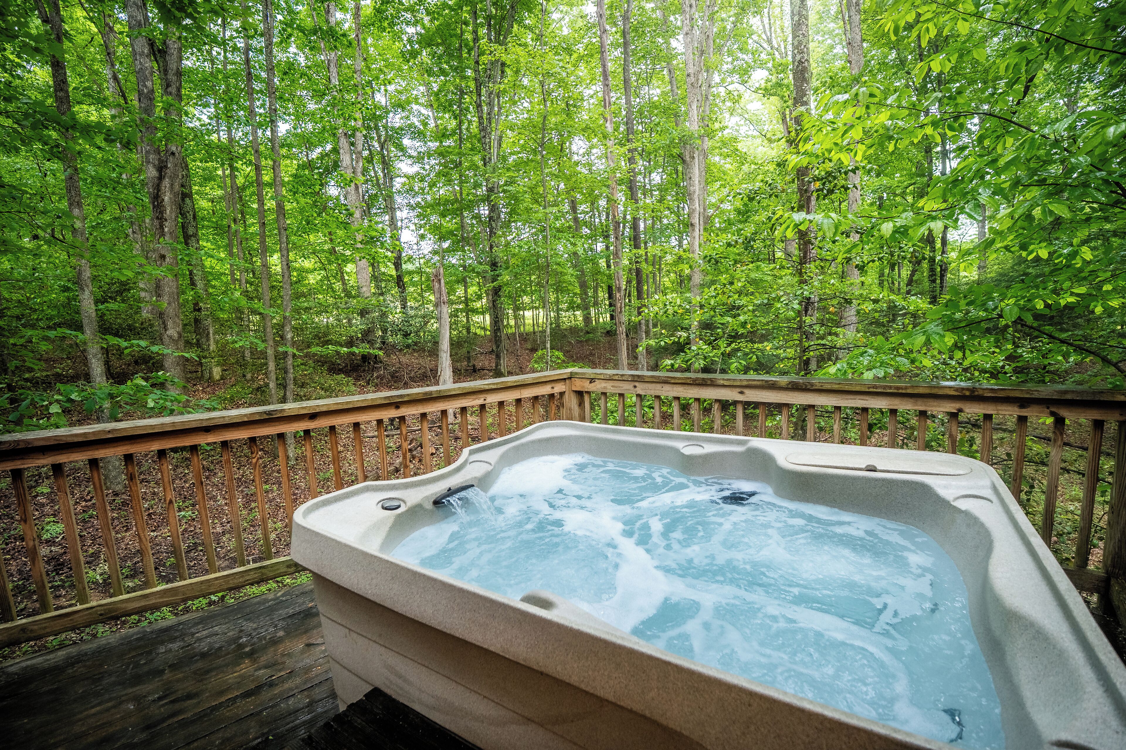 Un bain à remous entouré d’une terrasse en bois et bordé d’une zone boisée.