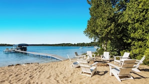 A beach with white lounge chairs, a dock extending into the water, and a clear blue sky.