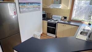 Eine kompakte Küche mit einer zentralen Kochinsel, zwei Barhocker, einem Kühlschrank, einem Backofen und einer Spüle.