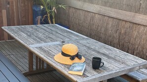 Eine Holzterrasse mit Picknicktisch und Bänken, ein Hut, ein Buch und eine Tasse.