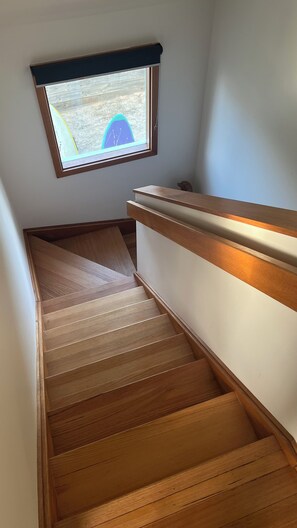 Una escalera de madera con barandilla y un ventanal arriba.