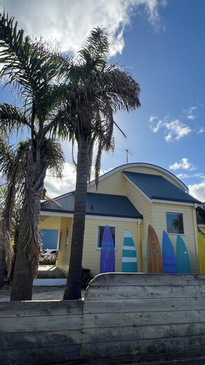 Une maison de plage avec un toit incurvé, un palmier et des planches de surf colorées exposées à l’extérieur.