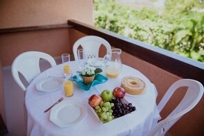A table set for breakfast with plates, cutlery, a pitcher of orange juice, a basket of fruit, and a donut on a balcony with white chairs. - BEST OF GUARAJUBA, GENIPABU SUMMER HOUSE, BEACHFRONT (Camaçari)