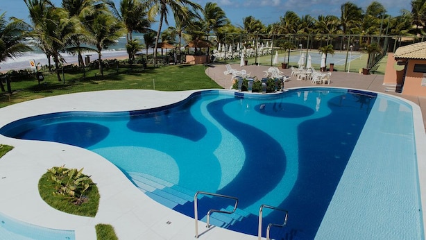 Una piscina con diseño ondulado, rodeada de palmeras y una cancha de tenis.