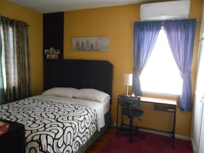 Een hotelkamer met een bed, een bureau met stoel, een raam met gordijnen en een schilderij aan de muur.