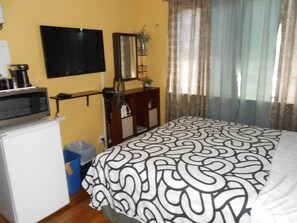 Une chambre à coucher comprenant un lit, une télévision, un four à micro-ondes et une petite poubelle.