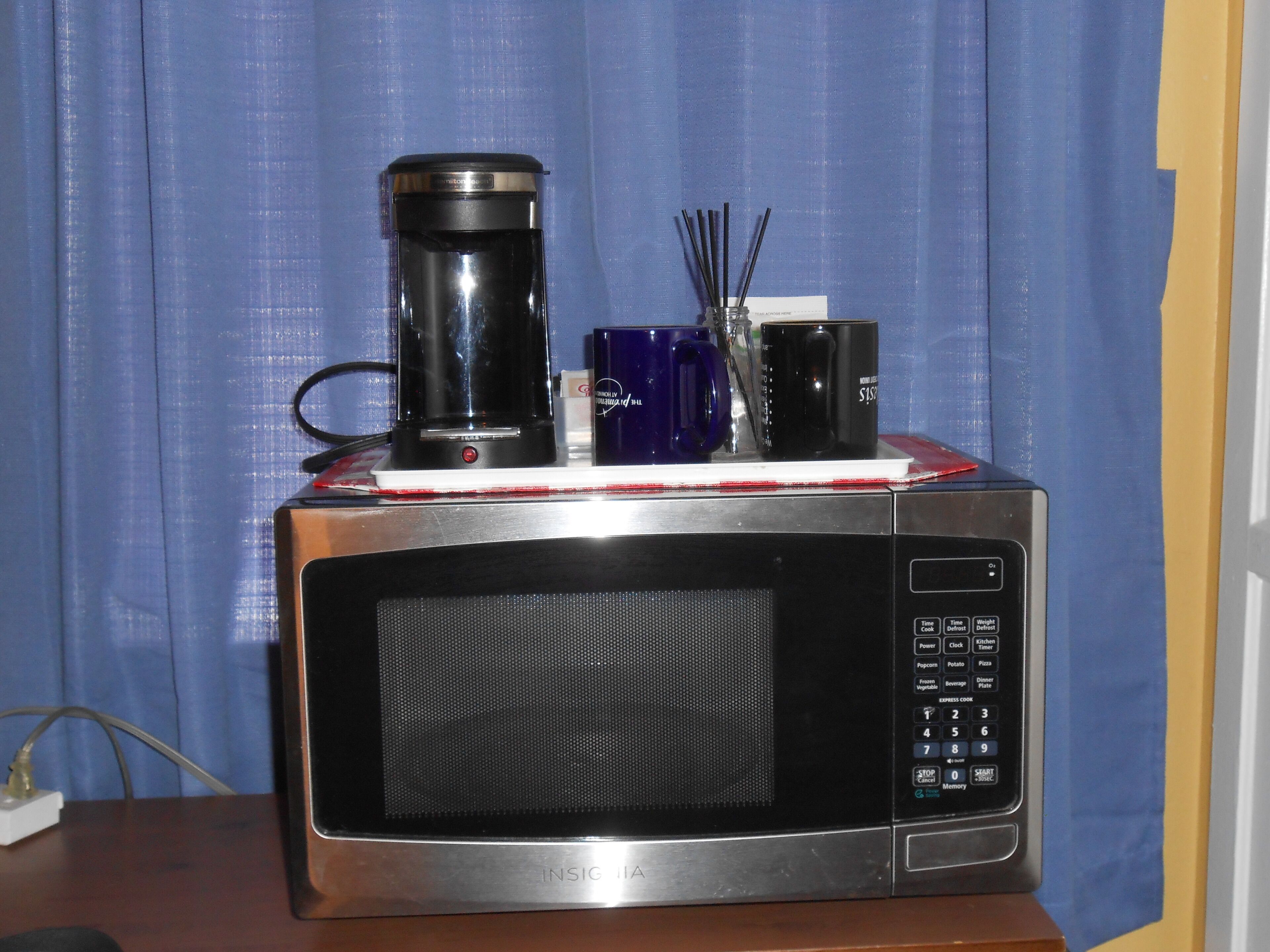A microwave with a coffee pot and a blue mug on top.