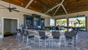 An outdoor bar area with a pool, bar stools, ceiling fans, and a view of the pool.