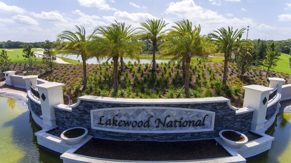 Un letrero con la leyenda "Lakewood National", mostrando un campo de golf y palmeras al fondo.