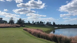 A golf course with a pond, trees, and a clear sky.
