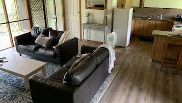 A living room with a sofa, a coffee table, and a rug. There is a kitchen area with a sink and a refrigerator.