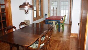 A dining room with a wooden table and chairs, a chandelier, and a view of the outside through a door. - The Mill House, year around Country Home & Historic Grist mill w/ 2 Kayaks (Posen)