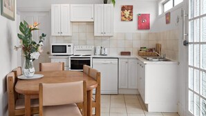 A modern kitchen with white cabinets, a dining table with chairs, a microwave, an oven, and a sink. - Apartment 1 - The Coachhouse (Sydney)